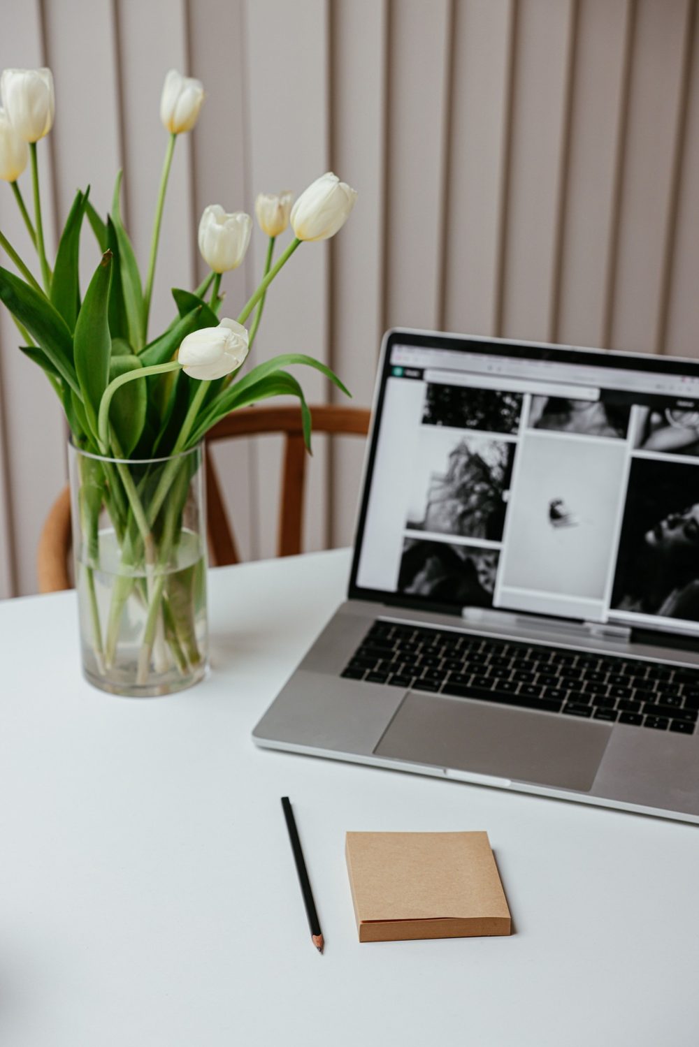 White tulips beside a laptop and notepad on a bright desk